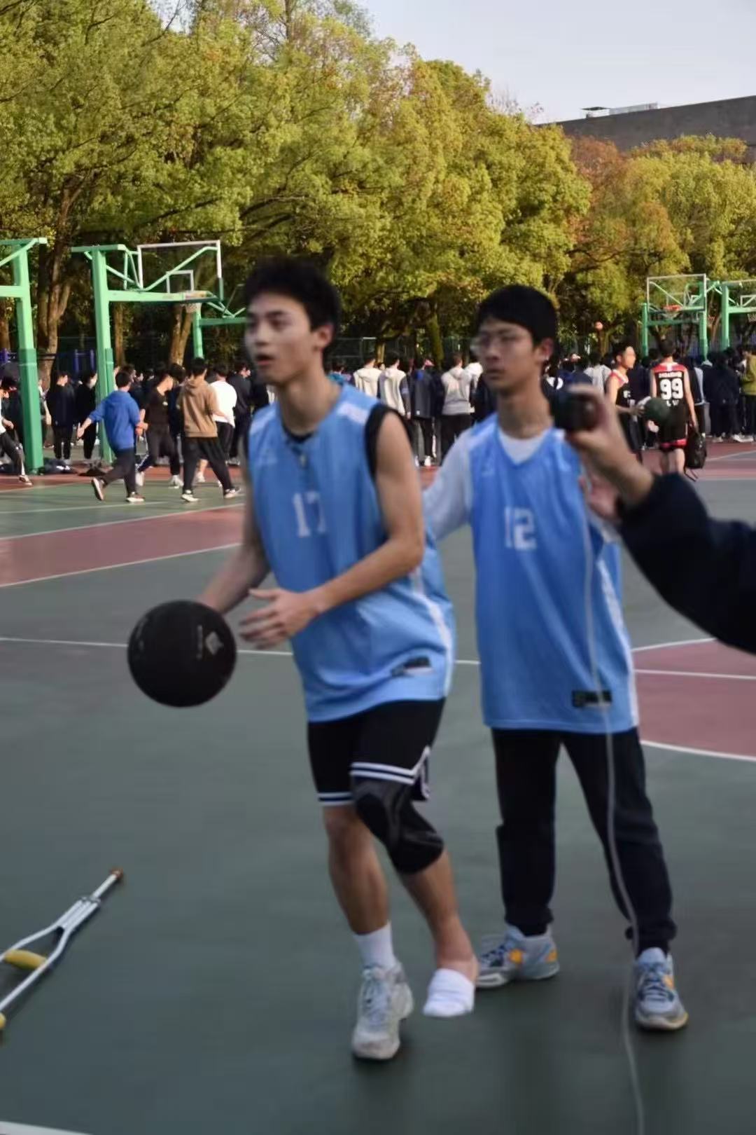 A player in a blue jersey standing on an outdoor court with crutches nearby